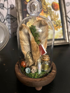 Antique doll head mounted on bone art, surrounded by faded playing cards and eerie shadows.